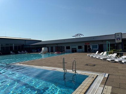 Freibad Winsen (Aller) Leeres Freibad bei Sonnenschein, mit Liegestühlen und einem Gebäude im Hintergrund.