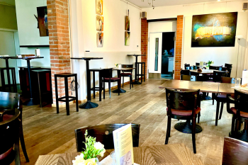 Kunstausstellung im nebenan Innenansicht des KulturCafés 'nebenan' mit Holzböden, Backsteinwänden, hohen Stehtischen und gemütlichen Sitzbereichen. Kunstwerke zieren die Wände des Cafés, in dem Veranstaltungen stattfinden.