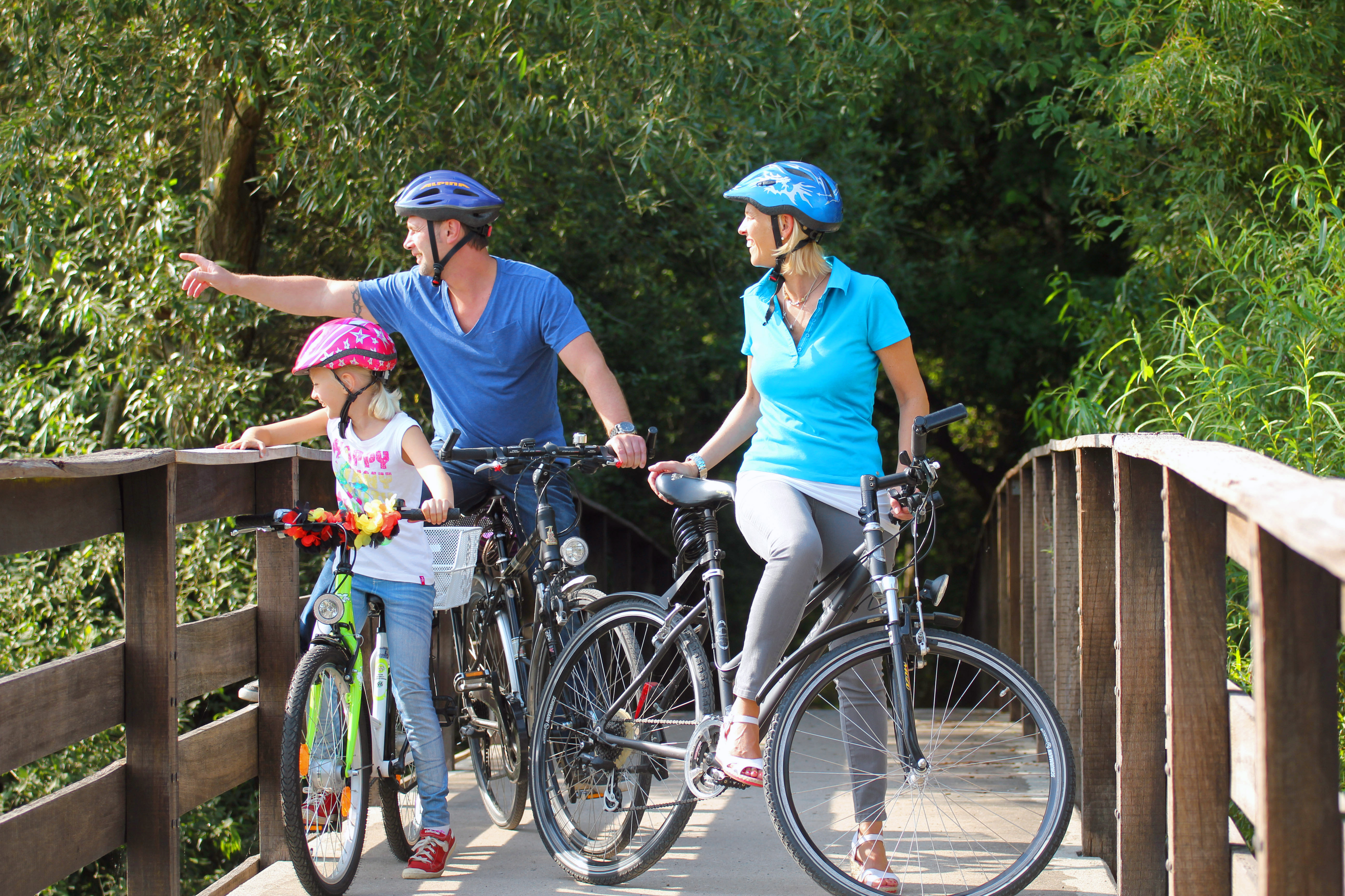 Familie mit Fahrrädern auf einer Holzbrücke im Grünen.